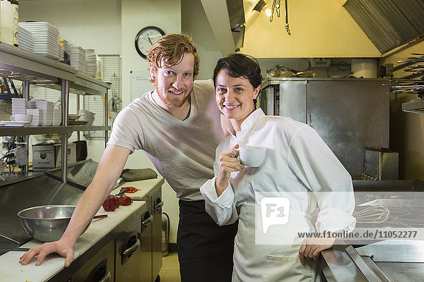 Caucasian chef and waiter smiling in restaurant kitchen