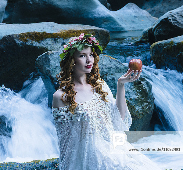 Kaukasische Frau hält Apfel am Wasserfall eines Flusses