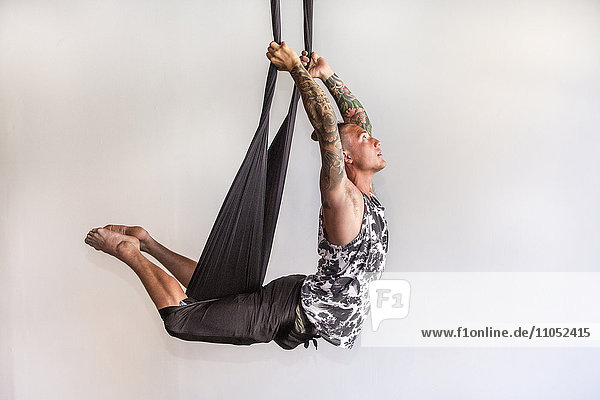 Gemischtrassiger Mann  der an Seilen hängend Yoga macht