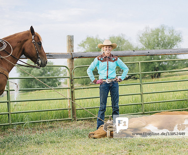 Cowgirl lächelt mit angebundenen Rindern auf einer Ranch