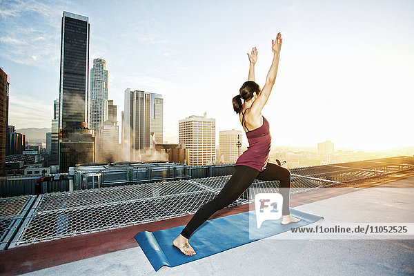 Gemischtrassige Frau übt Yoga auf einem städtischen Hausdach