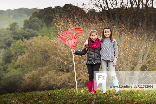 Mixed race sisters raking autumn leaves on lawn