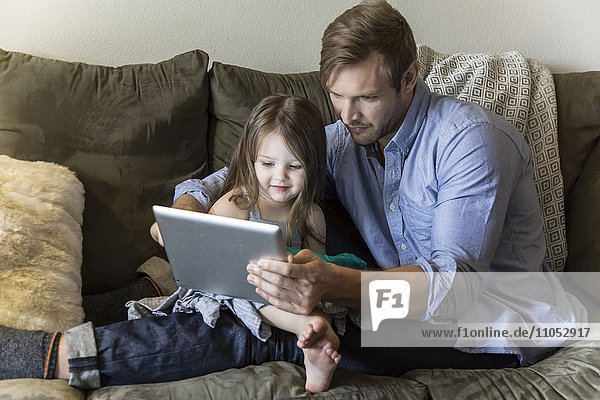 Vater und Tochter benutzen ein digitales Tablet auf dem Sofa