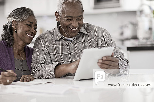 Ein älteres Ehepaar sitzt nebeneinander an einem Tisch  benutzt ein digitales Tablett und schaut auf den Bildschirm.