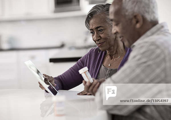 Ein grauhaariges Paar sitzt an einem Tisch und betrachtet Informationen auf einem digitalen Tablett.