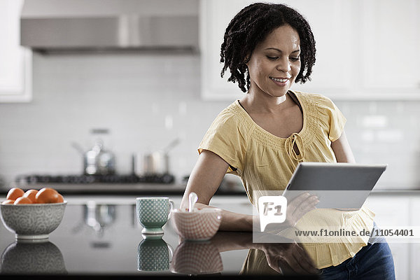 A woman using a digital tablet in her home. Standing in the kitchen.