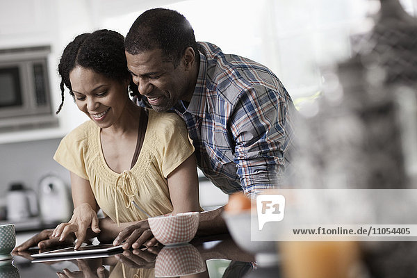 Ein Mann und eine Frau  ein Paar in der Küche  die beide auf ein digitales Tablet schauen.