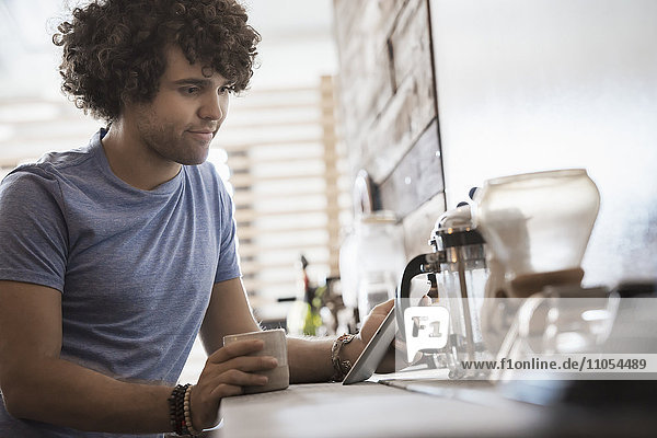 Loft living. A young man sitting with a cup of coffee  holding a digital tablet.