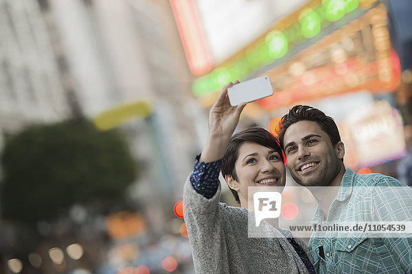A couple  man and woman on a city street taking a selfy with a smart phone.