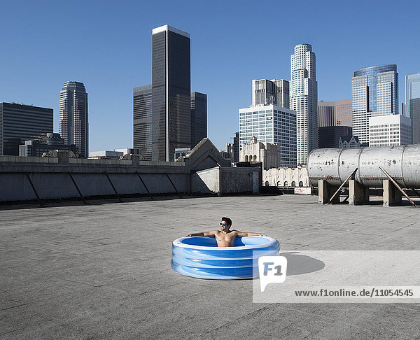 Ein Mann sitzt in einem kleinen aufblasbaren Wasserbecken auf dem Dach einer Stadt und kühlt sich ab.