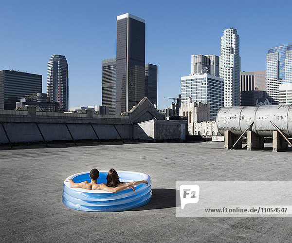 Ein Paar  ein Mann und eine Frau  sitzen in einem kleinen aufblasbaren Wasserbecken auf dem Dach einer Stadt und kühlen sich ab.