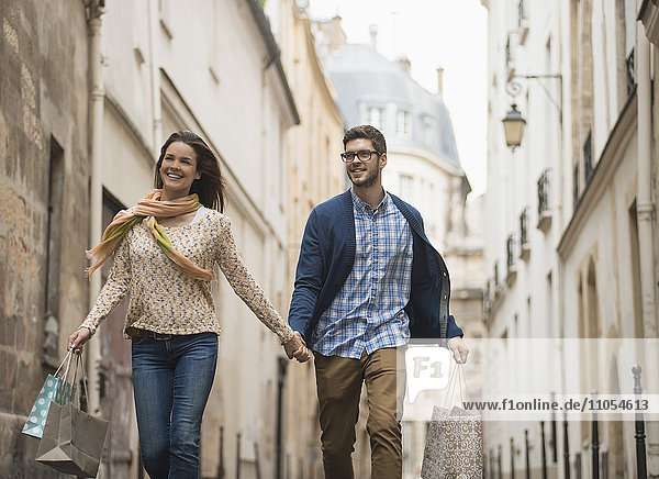 A couple walking along a narrow street in a historic city centre  with shopping bags.