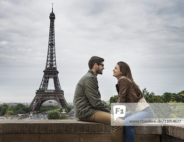 Ein Paar  das einander gegenüber an einer Wand in der Stadt Paris mit dem Eiffelturm im Hintergrund sitzt.
