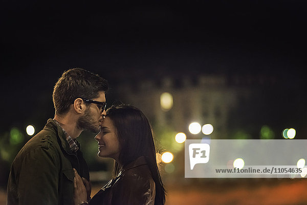 Ein Paar  das sich nachts in einer Stadt küsst.