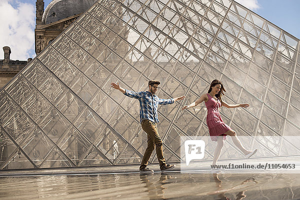 Ein Ehepaar im Hof des Louvre-Museums  bei der großen Glaspyramide. Springbrunnen und Wasser.