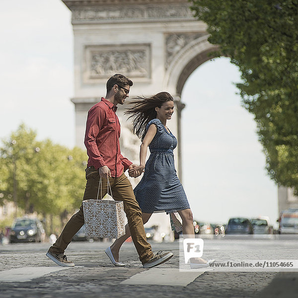 Ein Paar  das Hand in Hand Einkaufstaschen trägt und die Straße an einem historischen Denkmal im Herzen einer europäischen Stadt überquert.