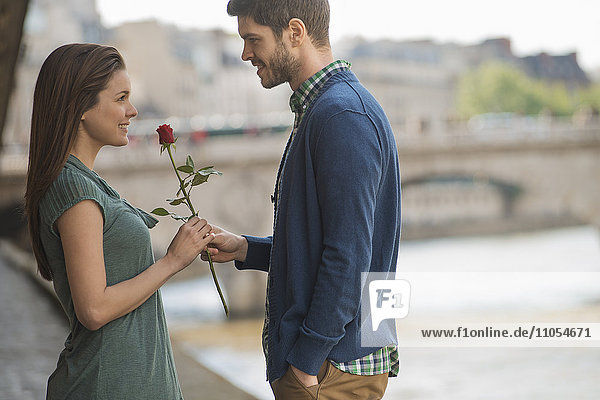 Ein Paar in einer romantischen Umgebung an einem Fluss. Ein Mann bietet einer Frau eine rote Rose an.