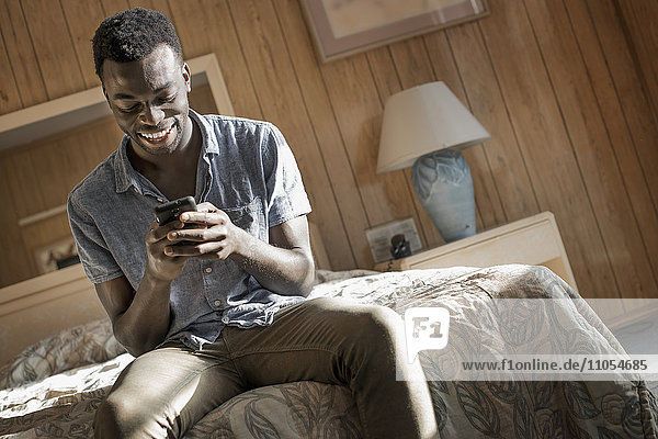 Ein junger Mann in einem Motelzimmer  der sein Smartphone überprüft.