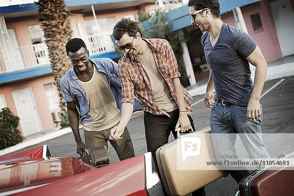 Drei junge Männer  Freunde  die das Auto mit Koffern und einer Gitarre für eine Autoreise packen.