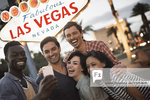 A group of five friends  men and women posing under the Las Vegas sign.