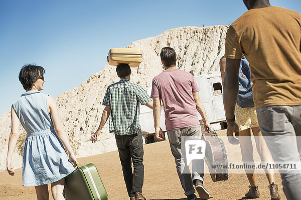 A group of people walking in a line in open desert country  carrying their cases  on a road trip.