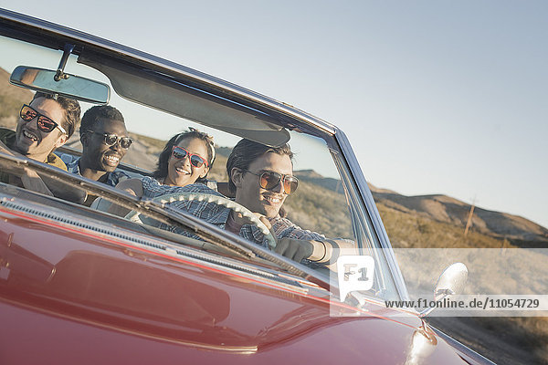 Eine Gruppe von Freunden in einem roten Cabrio-Oldtimer mit offenem Verdeck auf einer Autoreise.