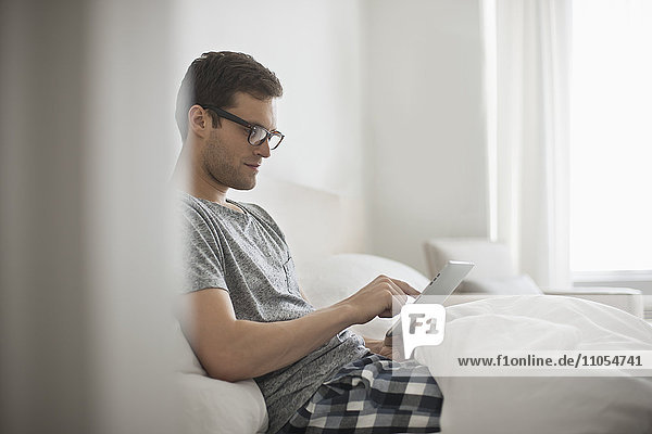 Ein Arbeitstag. Ein Mann sitzt im Bett und benutzt ein digitales Tablett mit Touchscreen.
