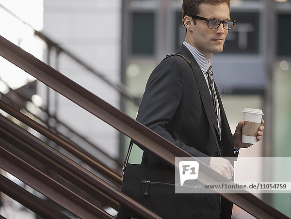 Ein Arbeitstag. Ein Geschäftsmann im Arbeitsanzug und mit Krawatte  der mit einer Tasse Kaffee die Treppe hinuntergeht.