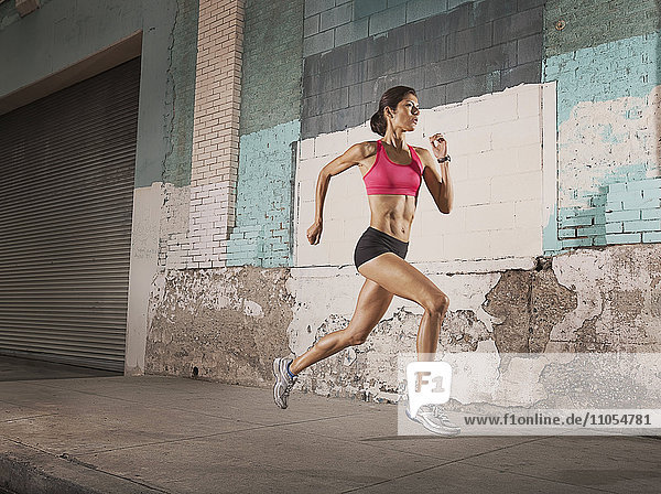 Eine Frau rennt eine städtische Straße entlang  vorbei an Gebäuden mit abblätternder Farbe und einem Metallfensterladen.