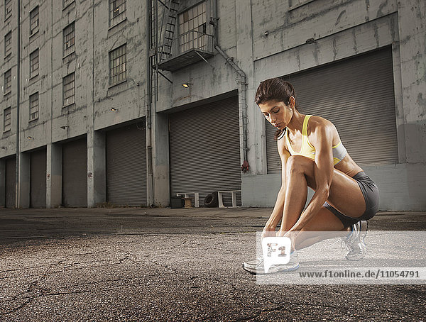 Eine Läuferin lehnt sich hinunter und bindet sich die Schnürsenkel ihrer Laufschuhe.