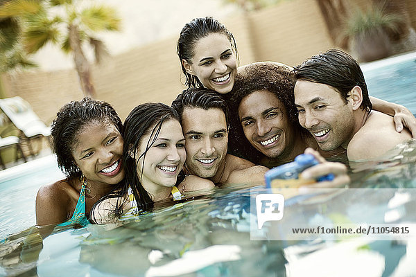 Eine Gruppe junger Männer und Frauen im Schwimmbad am Ende eines heißen Tages  die für ein Selfy posieren.