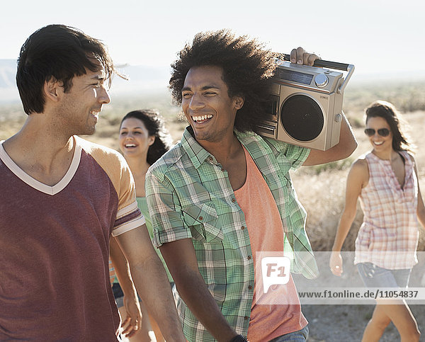 Group of young people  men and women walking on the open road with a boombox.