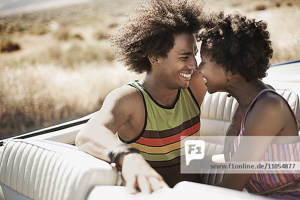 Ein junges Paar  Mann und Frau in einem hellblauen Cabriolet  auf dem Rücksitz dicht nebeneinander lachend.
