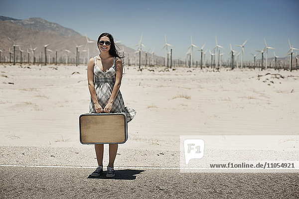 Eine junge Frau mit einem Koffer steht am Rand der Autobahn.
