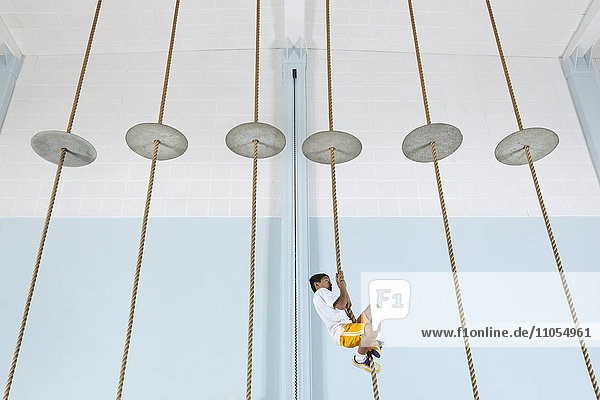 Ein Junge klettert in der Turnhalle an einem Seil hoch.