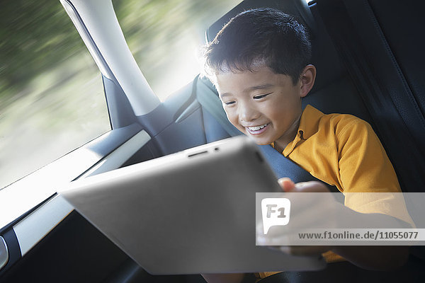 A boy travelling in the back seat of a car using a digital tablet.