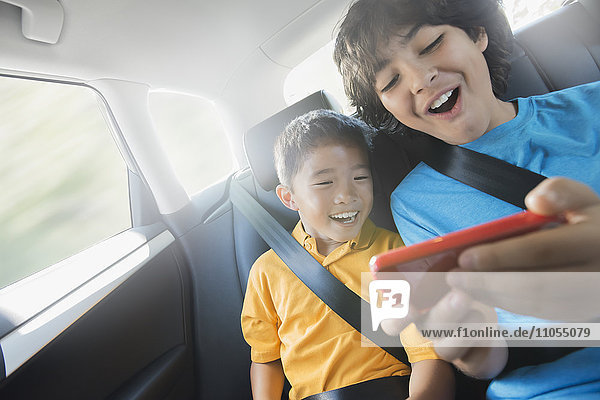 Zwei Kinder  die auf dem Rücksitz eines Autos reisen und sich ein tragbares Spieltablett teilen.