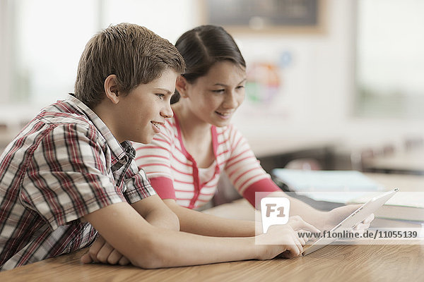 Zwei Kinder  ein Junge und ein Mädchen  sitzen in der Klasse und teilen sich ein digitales Tablett.