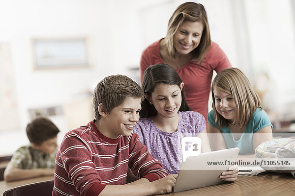 Eine Gruppe von Schülern im Unterricht und ein erwachsener Lehrer betrachten ein digitales Tablett.