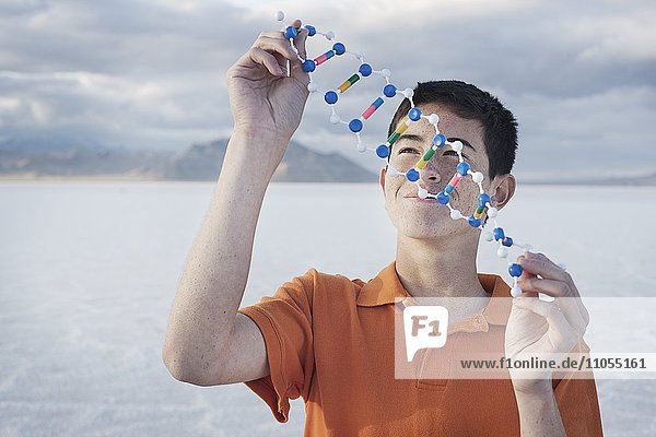 Ein Teenager in einem orangefarbenen Polohemd hält ein Molekularstrukturmodell und untersucht es.