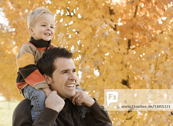 Ein erwachsener Elternteil und ein Kind  Vater und Sohn unter einem Baldachin aus orangefarbenem Herbstlaub.