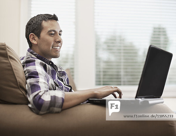 Ein Mann sitzt auf einem Sofa und benutzt einen Laptop-Computer.