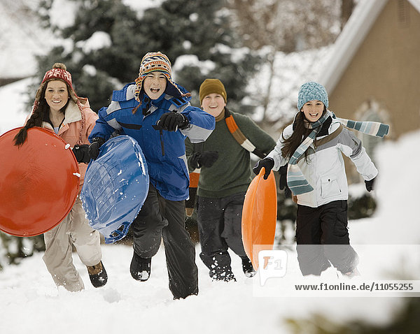 Schnee im Winter. Vier Kinder  Jungen und Mädchen  rennen mit Schlitten über den Schnee.