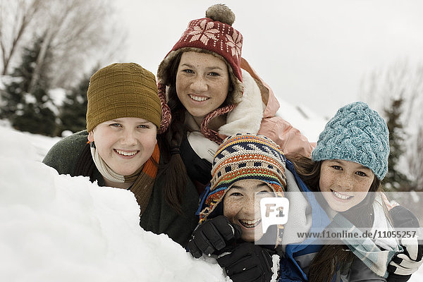 Schnee im Winter. Vier Kinder gruppierten sich lachend an einer Schneebank.