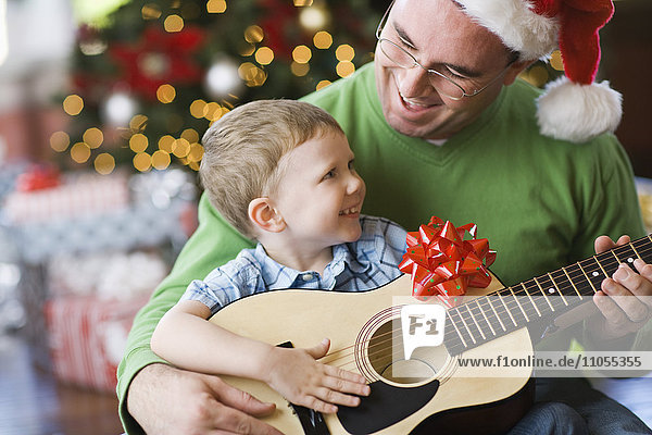 Ein Vater und sein Sohn sitzen an einem Weihnachtsbaum und spielen Gitarre.