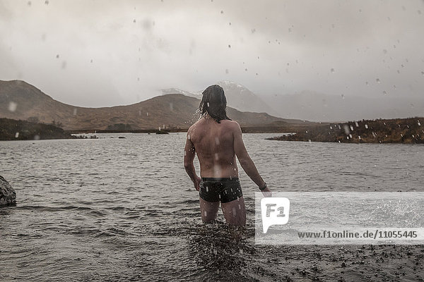 Ein Mann  der in Badehose mit den Oberschenkeln tief im Meerwasser steht.