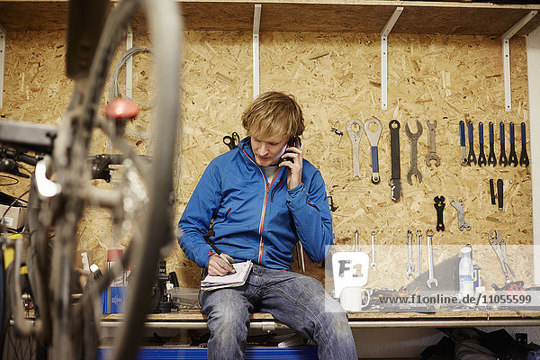 A young man using his smart phone in a cycle shop  making a call.
