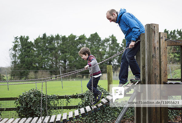 A boy and his father on a climbing frame  balancing on a gangway.