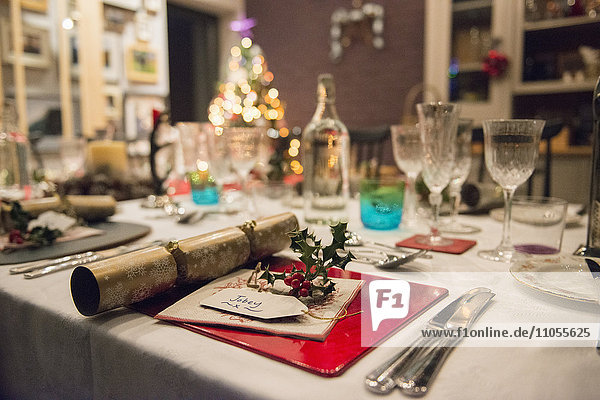 Ein gedeckter Tisch für ein Weihnachtsessen  mit Silber- und Kristallgläsern und einem Weihnachtsbaum im Hintergrund.