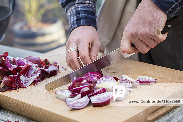 Ein Mann  der mit einem Messer Gemüse auf einem Brett hackt und rote Zwiebeln in Scheiben schneidet.